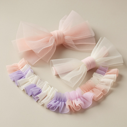 Composition en studio montrant plusieurs accessoires de mode délicats réalisés en tulle translucide rose poudré, ivoire et lavande.